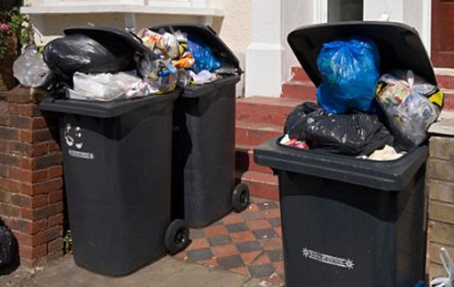 Picture of 3 very overflowing bins in front of a terraced house blocking the entrance. 